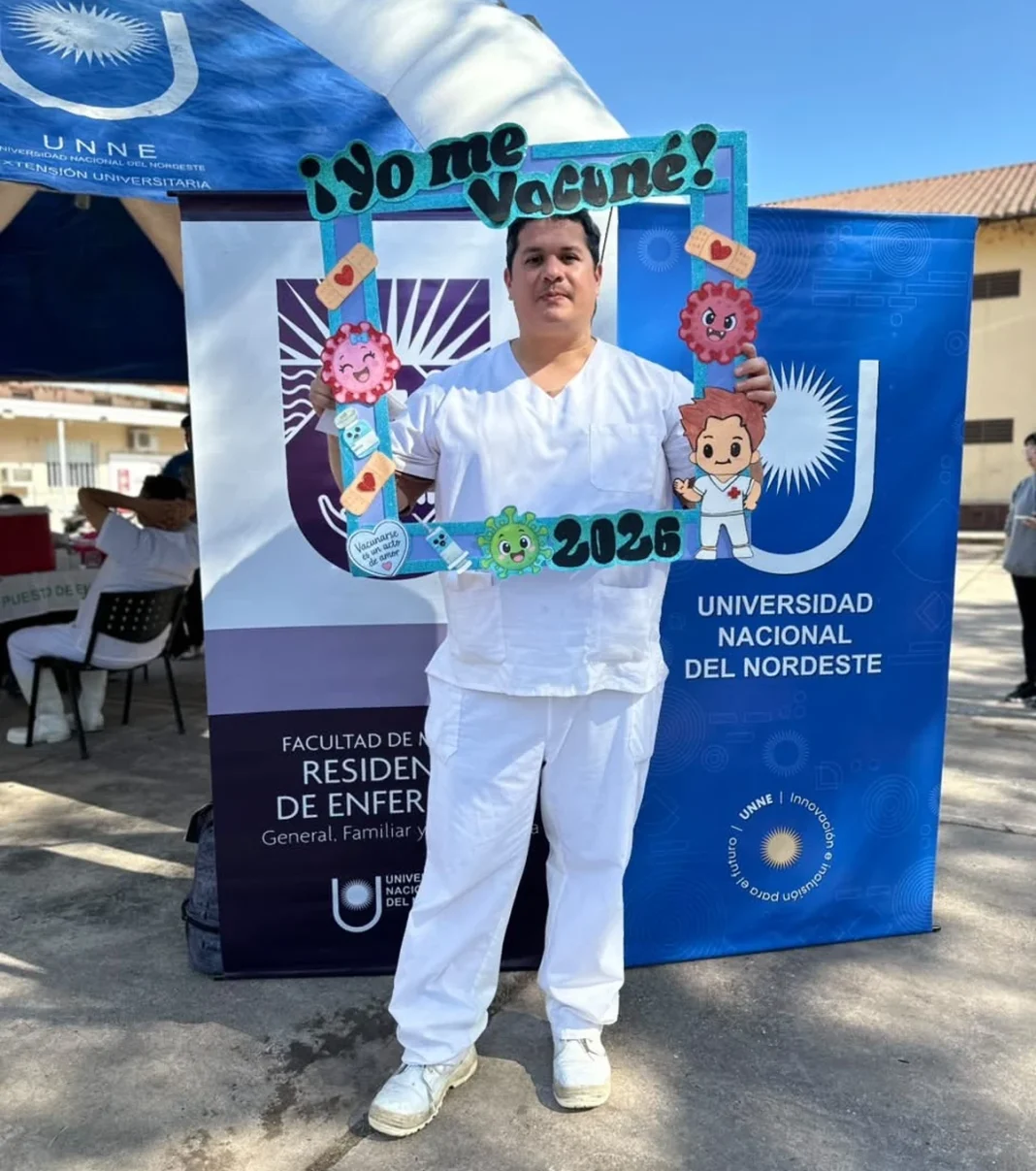 Trabajador de salud junto a un cartel de vacunación de la UNNE