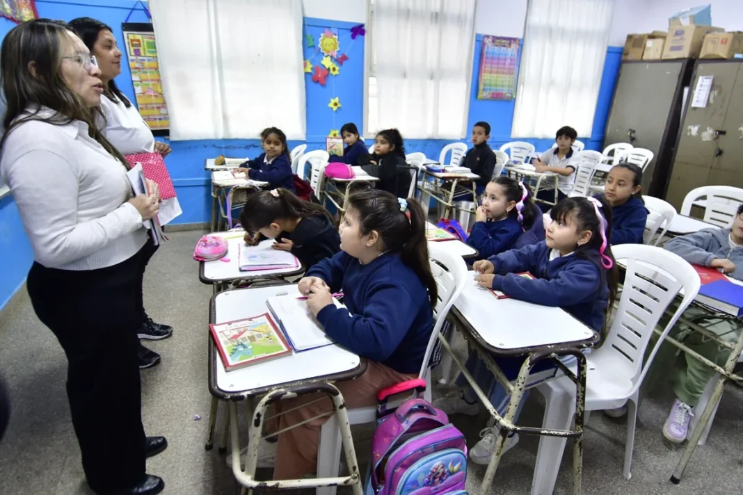 Una docente acompaña a estudiantes durante una actividad de lectura en un aula primaria.