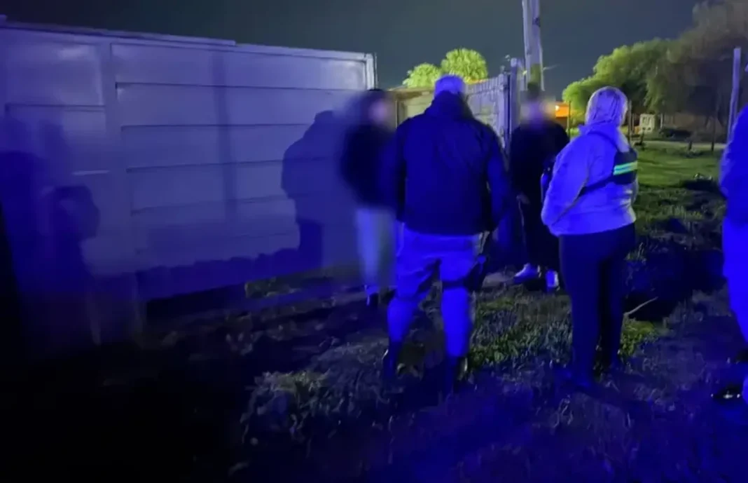 Dos personas junto a un vehículo durante un operativo nocturno iluminado por luces azules.