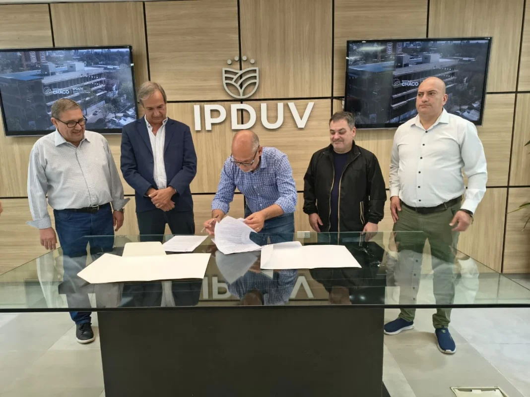 Un funcionario firma documentación del convenio ante representantes del IPDUV y la SUOPE.